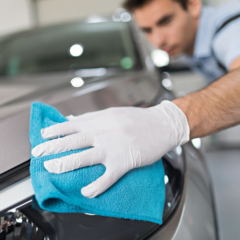 Ein hellblaues mikrofaser tuch wischt die glänzende schwarze oberfläche eines autos mit hygienorm safe fit weißen nitril handschuhen 200 stück