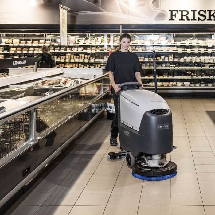 Nilfisk scheuersaugmaschine ba551 cd in grau und schwarz mit blauem bürstenkopf und ladegerät im einsatz