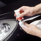 Rote und weiße sonax kratzerentfernerset lack tube wird mit kloth auf schwarzer fahrzeugoberfläche aufgetragen