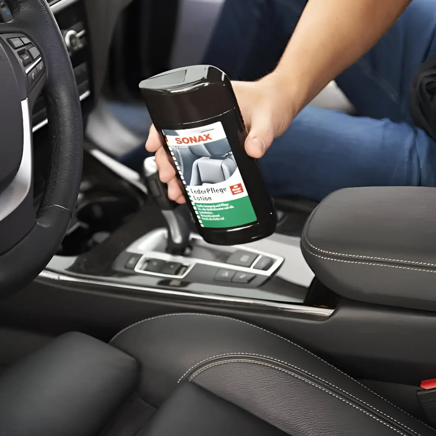 Hand hält schwarze Sonax LederPflegeLotion Flasche mit grün-weißem Etikett zur Lederpflege im Auto