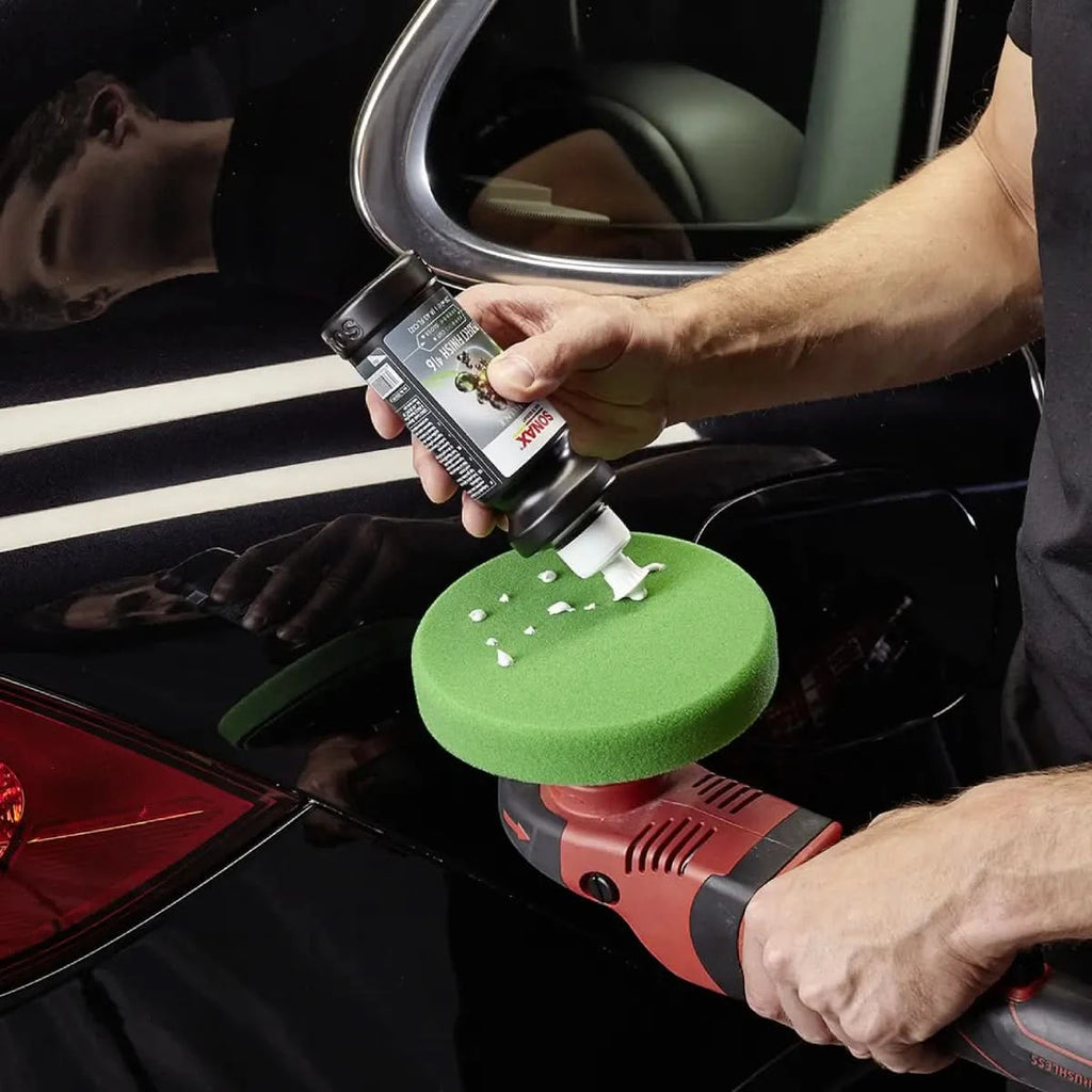 Schwarze meguiars ultimate polish flasche mit weißer applikatorspitze über grünem schaumstoffpolierpad am elektrischen polierer