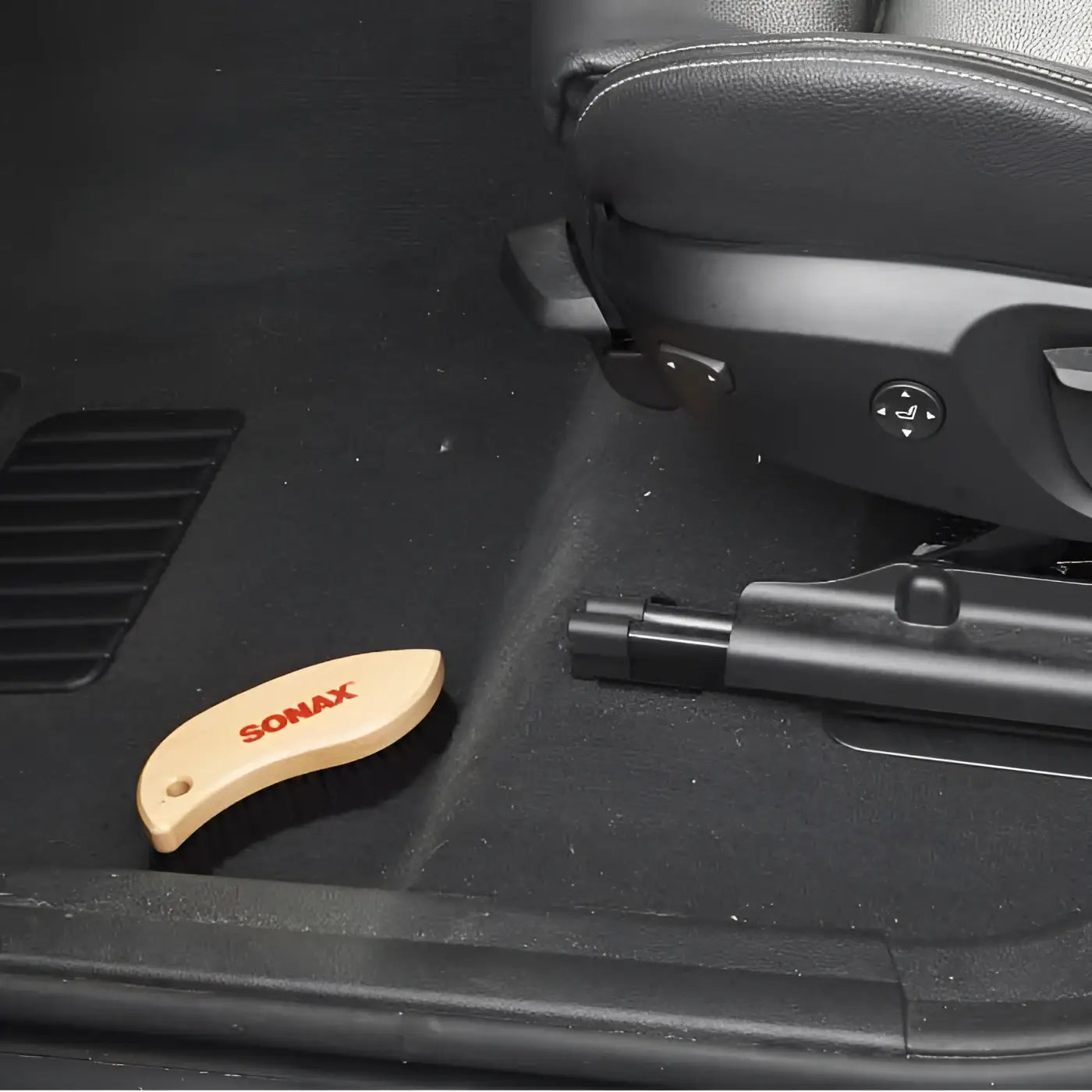 Eine hellfarbene holz-autobodenbürste aus sonax textil und lederbürste mit rotem sonax logo