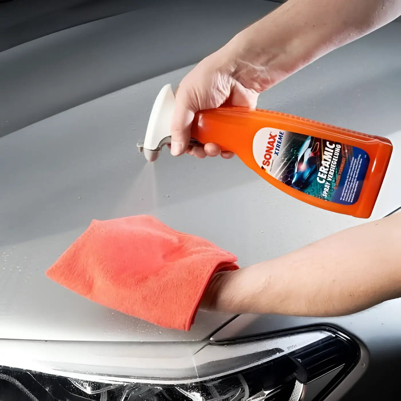 Orange sonax xtreme ceramic spray versiegelung 750ml mit weißer düse wird auf motorhaube aufgetragen