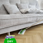 Swiffer anti-staub tücher trocken in grün und weiß auf holzboden unter grauem sofa liegend