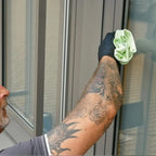 Ein hellgrünes mikrofasertuch aus dem unger ergotec fensterputzer-komplett-set 6in1 ak015 wird von einem schwarzen handschuh gehalten