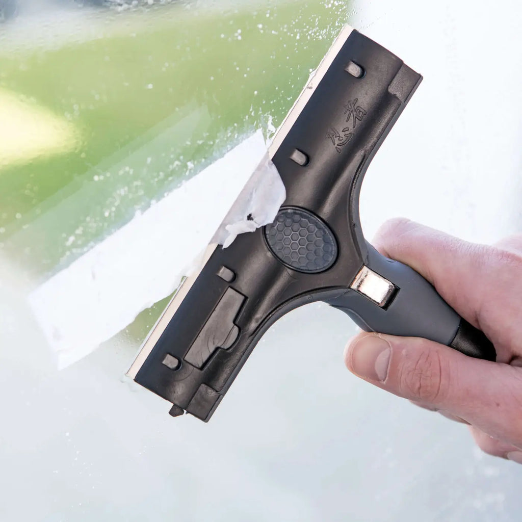 Schwarzer ungger ergotec ninja plastikrakel mit strukturierter griffzone und metallklinge zur kleberesteentfernung auf glas